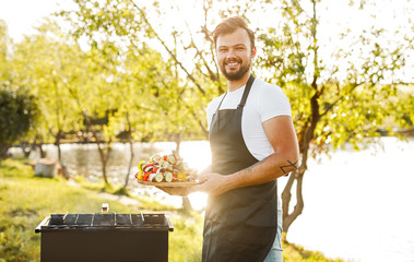 Cheerful chef with shish kebab during picnic