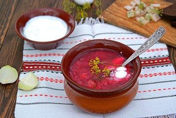 Borscht, hot soup with beets, cabbage and carrots in a clay bowl. Served with sour cream, rye bread and bacon.