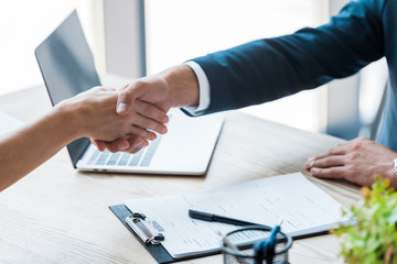 selective focus of employee and recruiter shaking hands near laptop