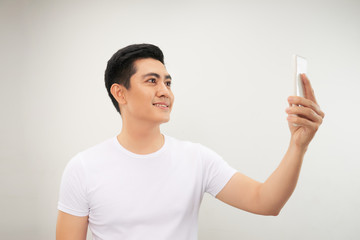 Smiling young asian man making selfie photo on smartphone over white background