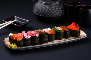 close up of sashimi sushi set with chopsticks and soy on black background. Korea rolls and green tea cups and teapot, copyspace.