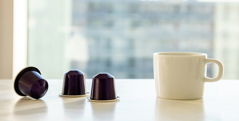 Espresso coffee cup and coffee capsules on a white table. Blur window background