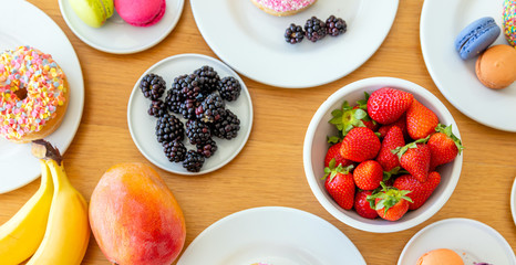 Colorful breakfast top view. Fresh fruits, donuts and macarons on wood. Banana, strawberry, blackberry and mango.