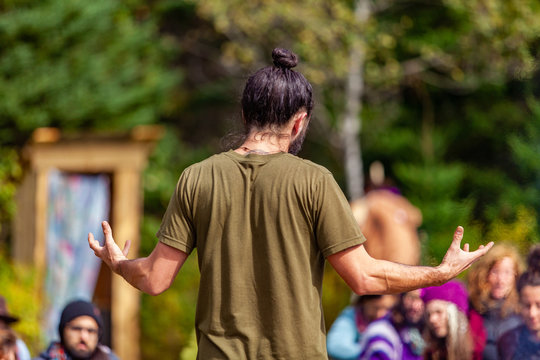 Fusion of cultural & modern music event. A spiritual guy dressed in bohemian style is seen giving a presentation at a campsite during a festival mixing native cultures and modern traditions