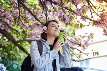 Young smiling happy woman hold green bottle on the background of blooming sakura
