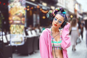 Cool funky hipster young woman with piercings and trendy sunglasses listening music on headphones outdoor - crazy look and hair