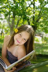Beautiful girl reading a book and lying on a hammock in the garden