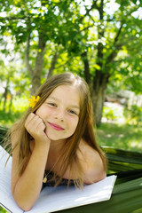 Beautiful girl reading a book and lying on a hammock in the garden