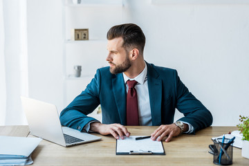 Naklejka premium confident recruiter sitting near laptop on wooden table
