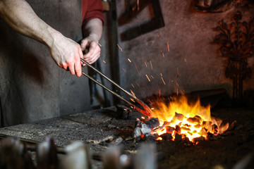 the work of a blacksmith in the forge. blacksmith holds red-hot metal by tongs in the forge furnace