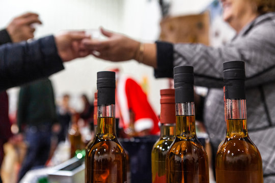 Seasonal products sold at Xmas market. Bottles of homebrewed mulled wine are seen close-up at a Christmas exposition, a shopper is seen exchanging money with a seller, blurry in the background.