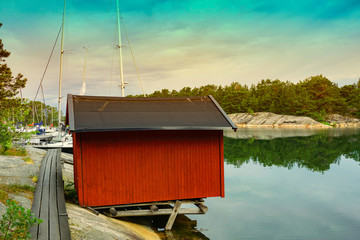 Fototapeta na wymiar Traditional red wooden house in the island with bridge at sunset clouds sky in Sweden