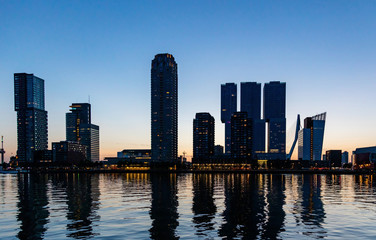 Fototapeta premium Rotterdam city Netherlands illuminated skyscrapers, reflections on the water, sunset time, blue clear sky
