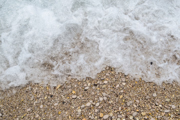 Sea foamy wave on a pebble beach top view