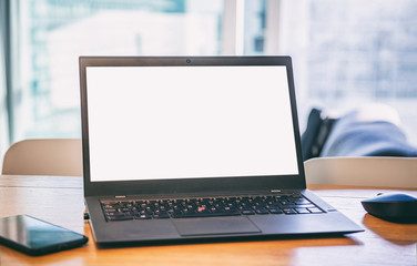 Blank screen laptop on a wooden desk, blur winddow background