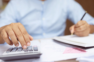 Obraz na płótnie Canvas Close up business man hand is writing in a notebook and using calculator counting making notes Accounting at doing finance at office. Savings finances concept. note pad. Leave space for writing text.