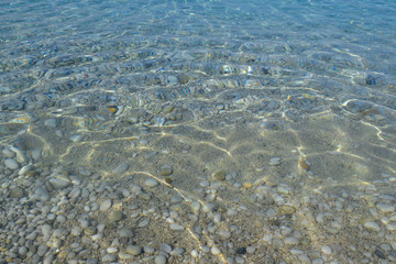 Stones in the sea water and ripples. Pebbles under water. Nautical background. Clean and transparent water. Mediterranean sea.