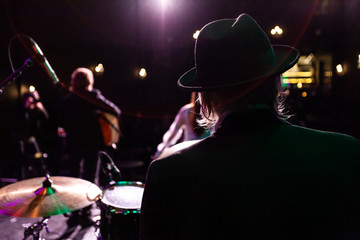 Musicians entertain people in night club. A rear view of a silhouetted man wearing a top hat as he...