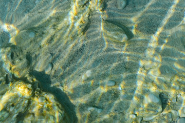 Top view of transparent clear water of river or creek with pebble stones. Abstract nature background