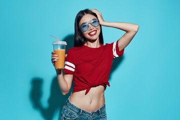 Relaxing with cold drink. Attractive young Asian woman smiling and looking at camera while standing against blue background