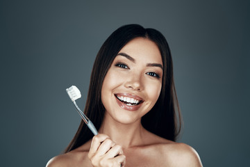 Morning routine. Beautiful young Asian woman smiling and looking at camera while standing against...