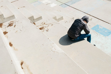 man curled up sitting on an outdoor stairway