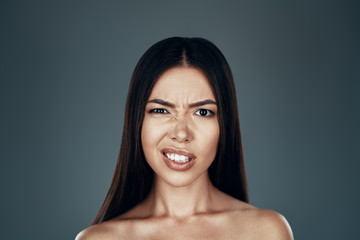 What? Confused young Asian woman making a face and looking at camera while standing against grey...