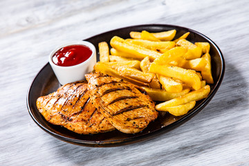 Grilled chicken fillets with french fries on wooden table