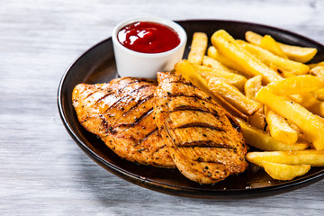 Grilled chicken fillets with french fries on wooden table