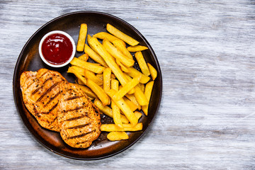 Grilled chicken fillets with french fries on wooden table