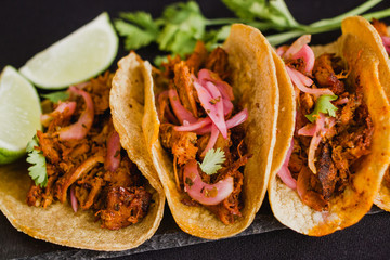 Close-up of Cochinita pibil tacos on a black background, with lime and coriander. Cochinita pibil...