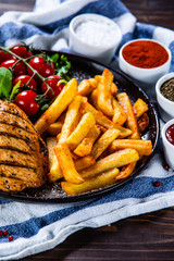 Grilled chicken fillet with french fries on wooden table