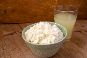 Liquid milk whey in a glass and cottage cheese in bowl on rustic wooden background. Dairy production