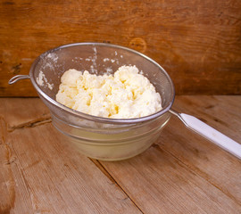 cottage cheese in strainer in bowl with Liquid milk whey on wooden background. Dairy production concept