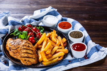 Grilled chicken fillet with french fries on wooden table