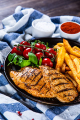 Grilled chicken fillet with french fries on wooden table