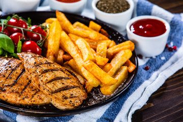 Grilled chicken fillet with french fries on wooden table