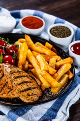 Grilled chicken fillet with french fries on wooden table