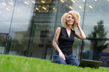 during break, young hipster girl. afro hair curls resting in park on grass near business center. Girl resting on lawn from working on laptop. Dream.