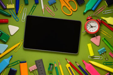 Modern digital tablet on a green background among office and school supplies. School office supplies on a desk with copy space. Back to school concept.