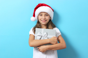 cute cheerful girl in a Christmas hat on a colored background holding a gift