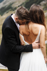 Young caucasian stylish groom kissing her bride on the shoulder.