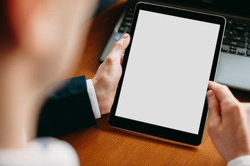 Close up of male hand using a tablet with white screen while sitting on a table indoor.