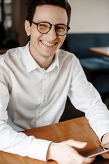 Close up portrait of an attractive young freelancer working at his tablet while sitting in a coffee shop looking at careem laughing .