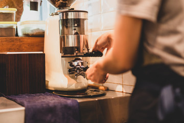 Fototapeta na wymiar Barista grinding fresh coffee beans using coffee machine.