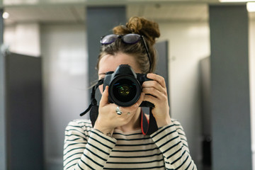 Atmosphere during corporate conference. A close up and front view of a young Caucasian woman taking a photograph behind a professional camera. Looking straight into the lens with room for copy.