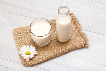 Obraz na płótnie Canvas Bottle and glass of milk, chamomile flower on gray background.