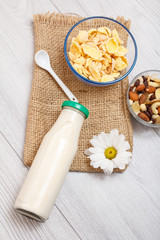 Glass bottle of milk, bowls with muesli and cornflakes on gray background