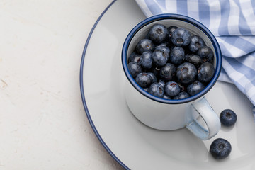 Close-up of fresh blueberries in white porcelain cup. Background with blue tones.