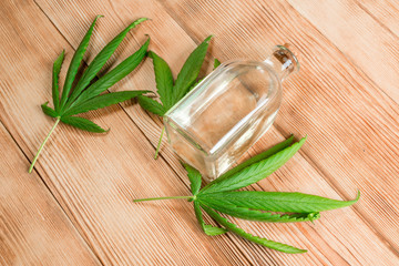 Balsam, elixir, hemp lotion. Fresh green leaves of marijuana and a bottle of liquid on a wooden background.
